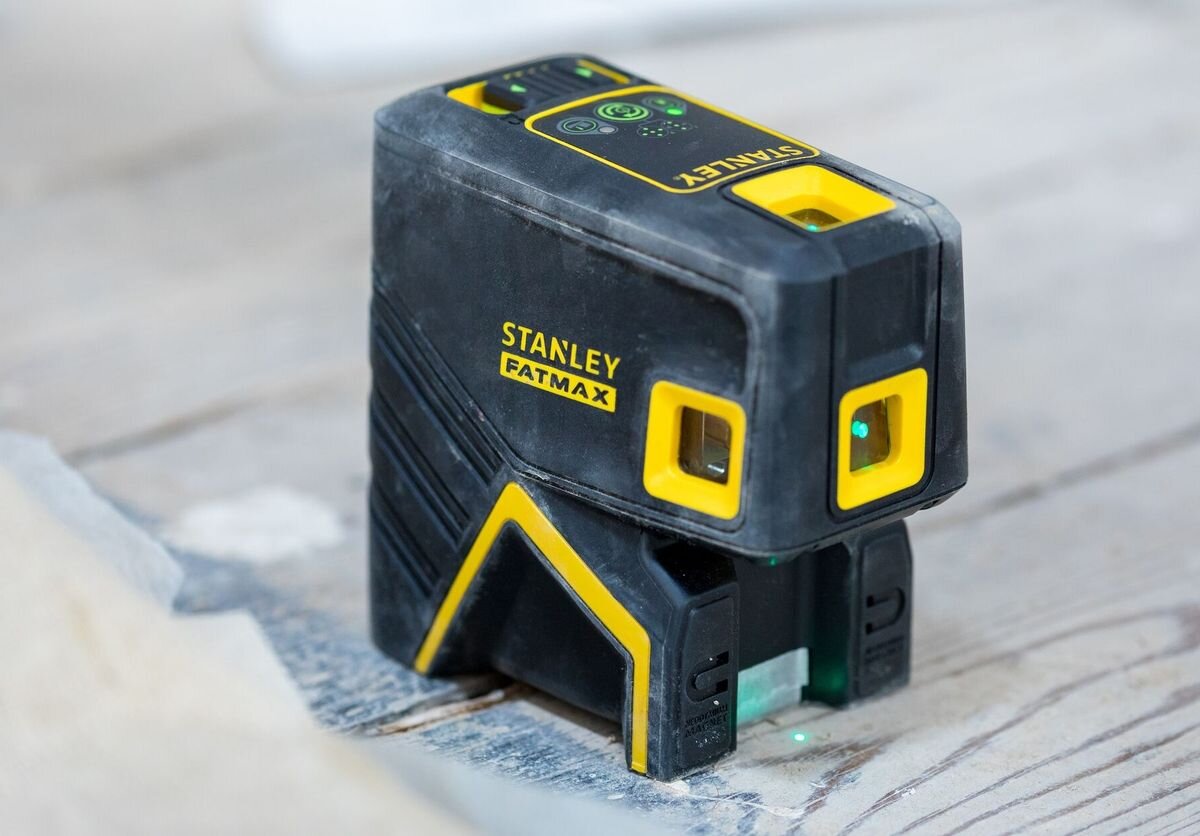 Laser krzyżowy STANLEY Fatmax FMHT77596-1, obudowa, pył, woda, trwałość, zbliżenie na laser stojący pionowo na panelach