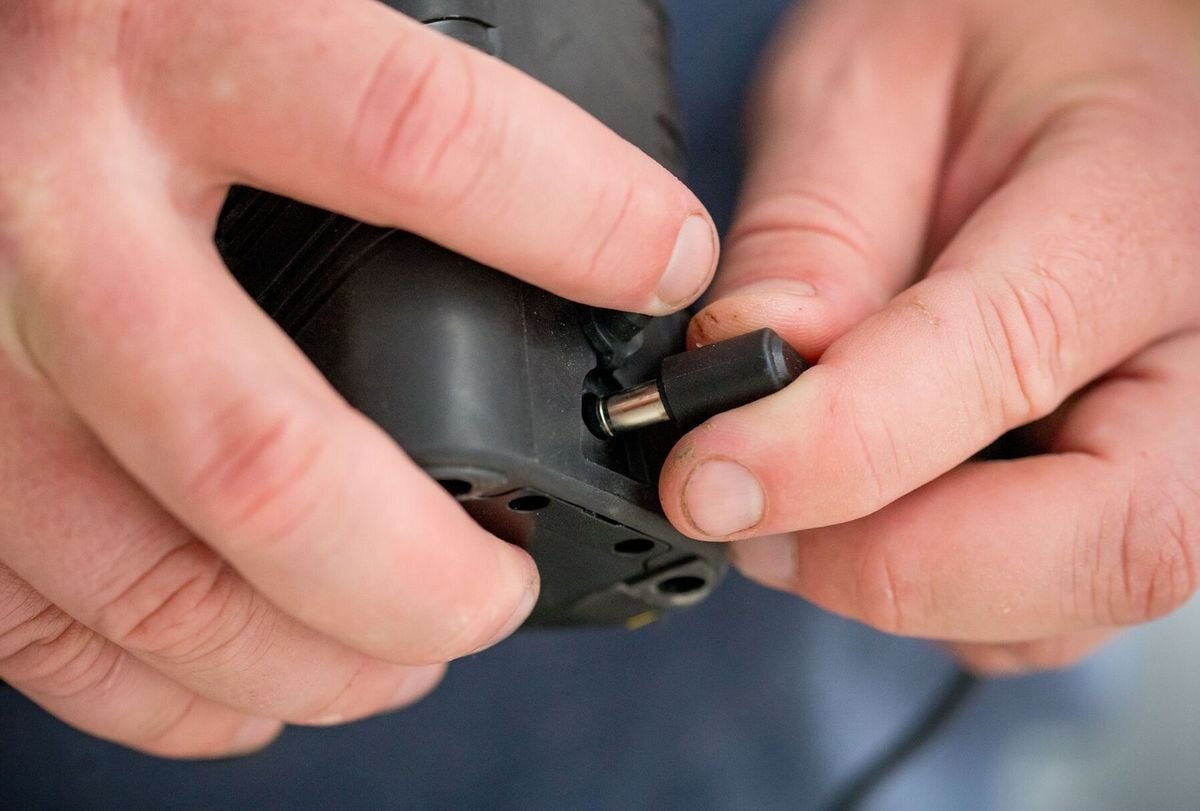 Laser krzyżowy STANLEY Fatmax FMHT77596-1, akumulator, ładowanie, prąd, energia, dłonie obsługują panel lasera zamontowanego do tripoda