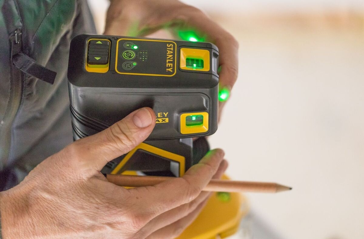Laser krzyżowy STANLEY Fatmax FMHT77596-1, statyw, gwint, montaż, uchwyt, dłonie obsługują uchwyt do lasera