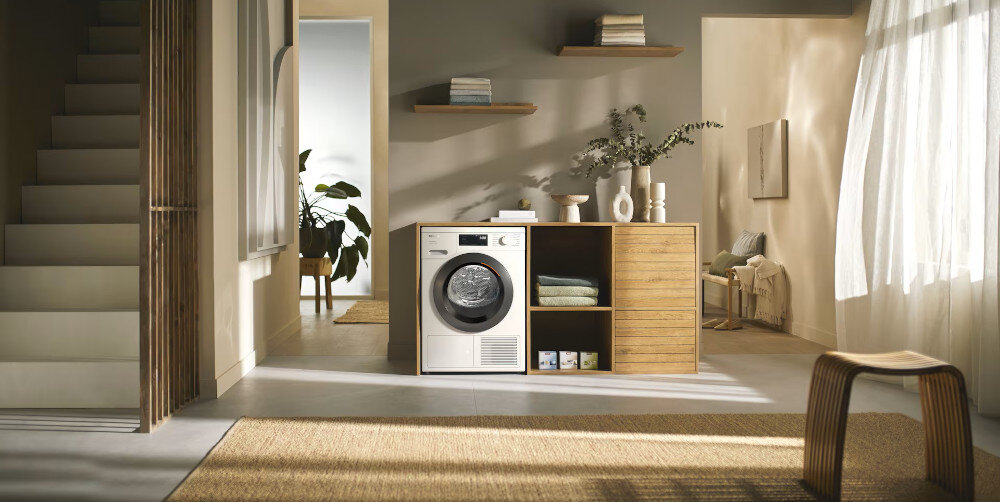 SUSZARKA MIELE TED645 WP wizualizacja suszarka front kolor biały w obudowie drewnianej salon półka ręczniki dekoracje stolik rośliny akcesoria Suszarka z pompą ciepła