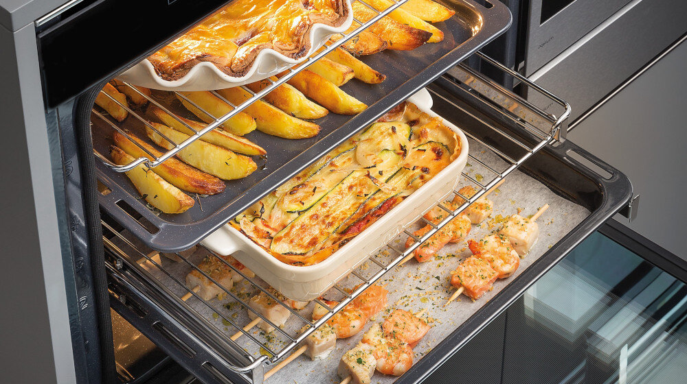 Wnętrze piekarnika z kilkoma potrawami pieczonymi jednocześnie na różnych poziomach. Grafika prezentuje funkcję równoczesnego pieczenia wielu dań COOK4