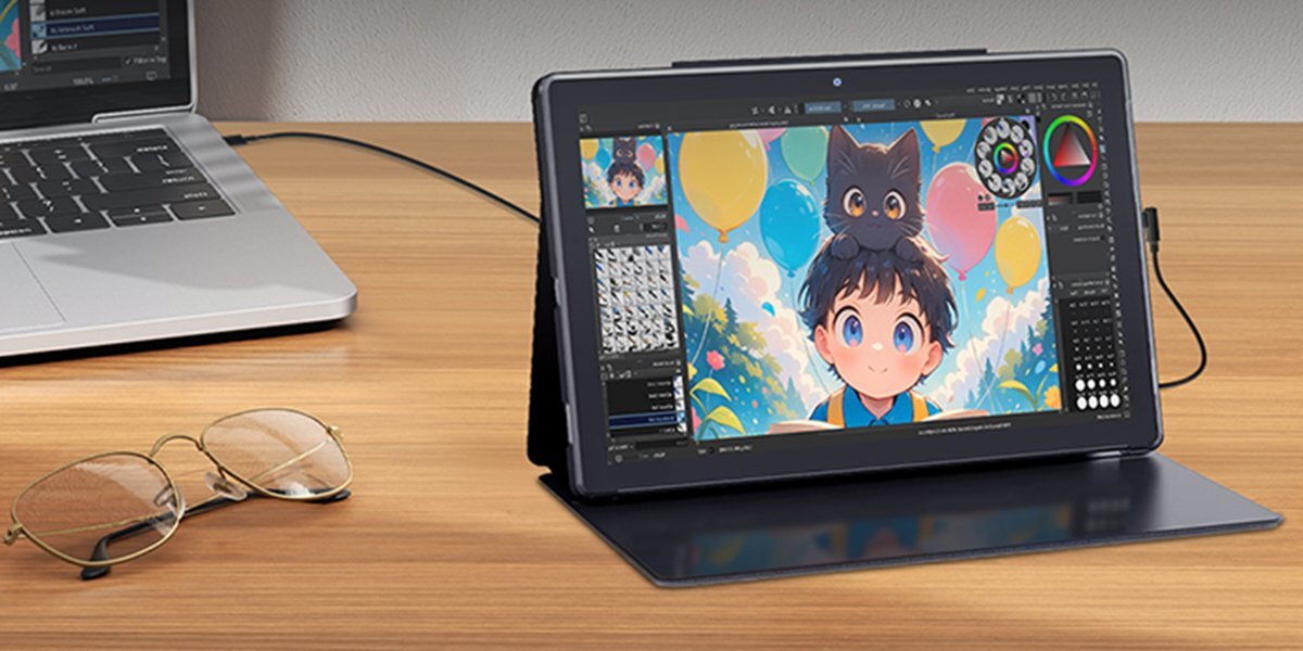 Tablet graficzny BOSTO ustawiony pionowo na biurku obok okularów oraz laptopa.
