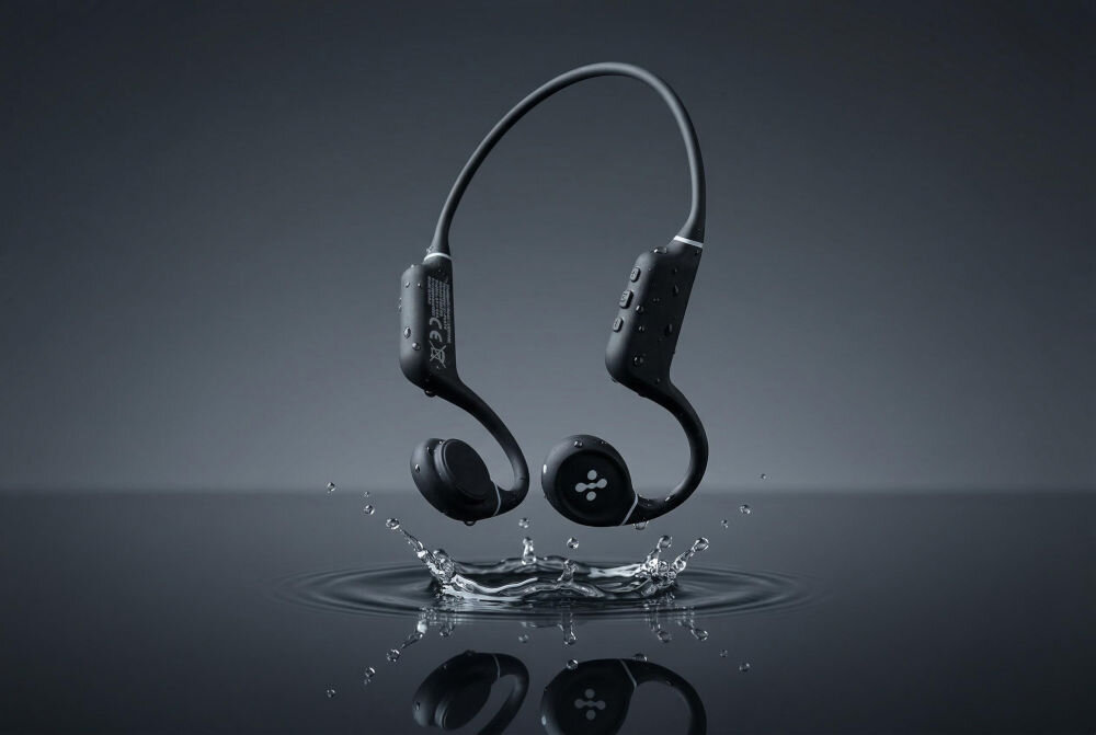 Słuchawki kostne XMUSIC XWS700K Swim – przewodnictwo kostne, technologia bone conduction, pływanie Artystyczne, studyjne ujęcie czarnych słuchawek z technologią przewodnictwa kostnego unoszących się nad lustrem czystej wody. Słuchawki odbijają się w wodzie, widać delikatne pluski i kropelki. Tło jest ciemnoszare, neutralne. Ujęcie podkreśla wodoodporność i design urządzenia