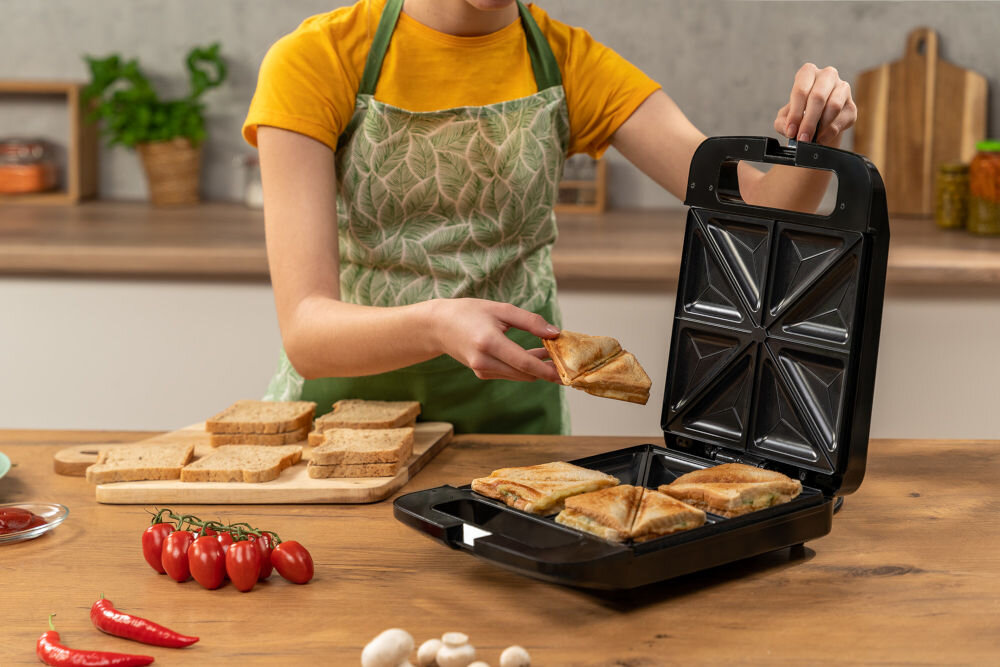 Opiekacz GOTZE & JENSEN SM703X zamknięty opiekacz stojący na drewnianym blacie w tle osoba przygotowywująca tosty