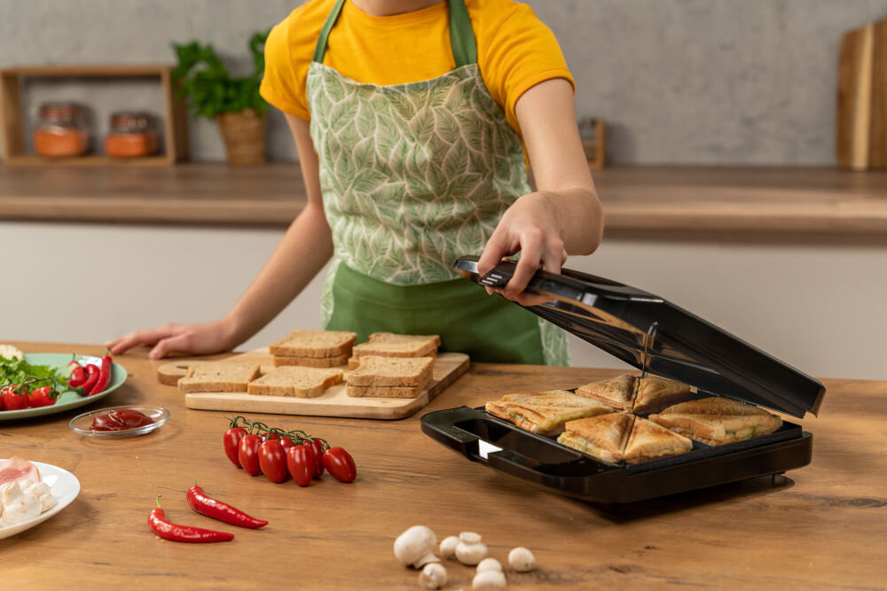 Opiekacz GOTZE & JENSEN SM703X osoba trzymająca uchwyt uchylonego opiekacza w środku pieką się tosty