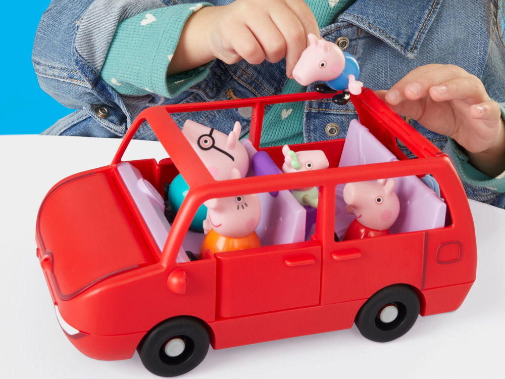Zestaw figurek HASBRO Świnka Peppa Duży pojazd G05415L0 Czerwony zabawkowy van Peppa Pig z otwartymi wszystkimi drzwiami i bagażnikiem, zaprezentowany na białej powierzchni na tle błękitnego nieba z rysunkami słońca i chmur. Przed autem ustawione są akcesoria: fioletowy fotelik, błękitna torba, figurka George'a i figurka Peppy.