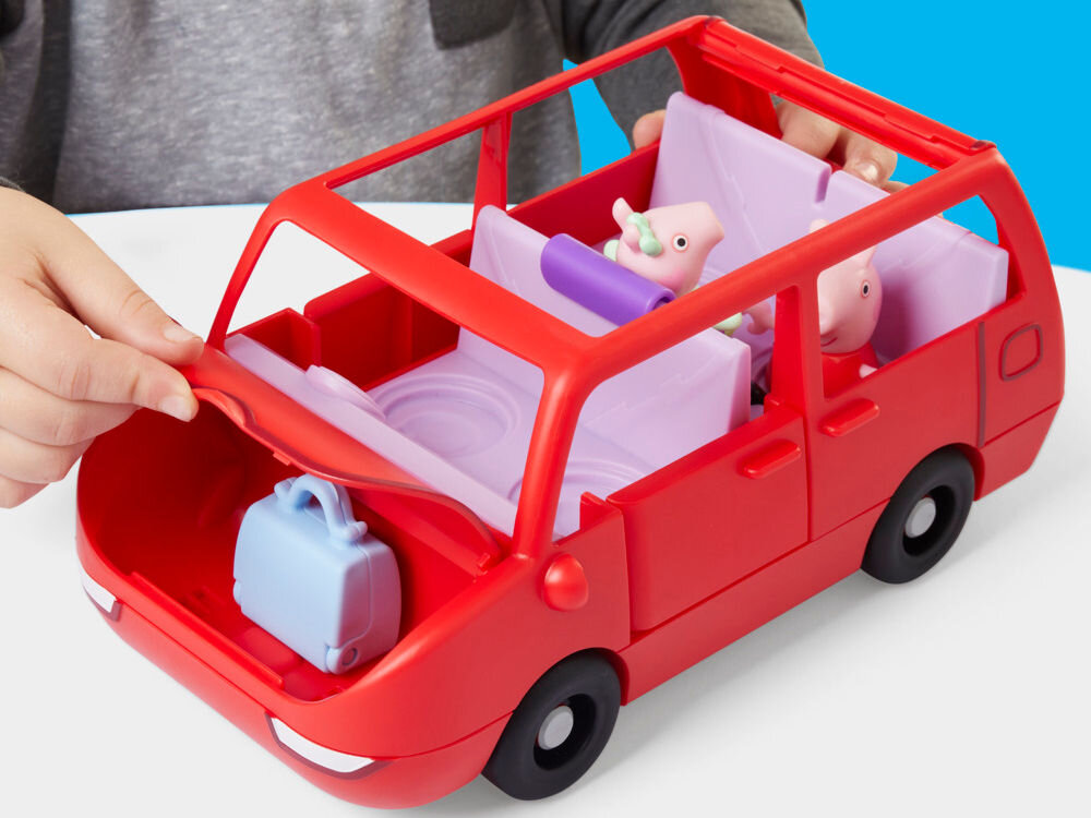 Zestaw figurek HASBRO Świnka Peppa Duży pojazd G05415L0 Widok od góry na otwarty czerwony zabawkowy van Peppa Pig. Ręka dziecka w szarej bluzce trzyma fioletowy fotelik samochodowy, unosząc go nad bagażnikiem, w którym znajduje się błękitna torba. Wnętrze auta ma fioletowe siedzenia z wytłoczeniami. Scena na białej powierzchni.
