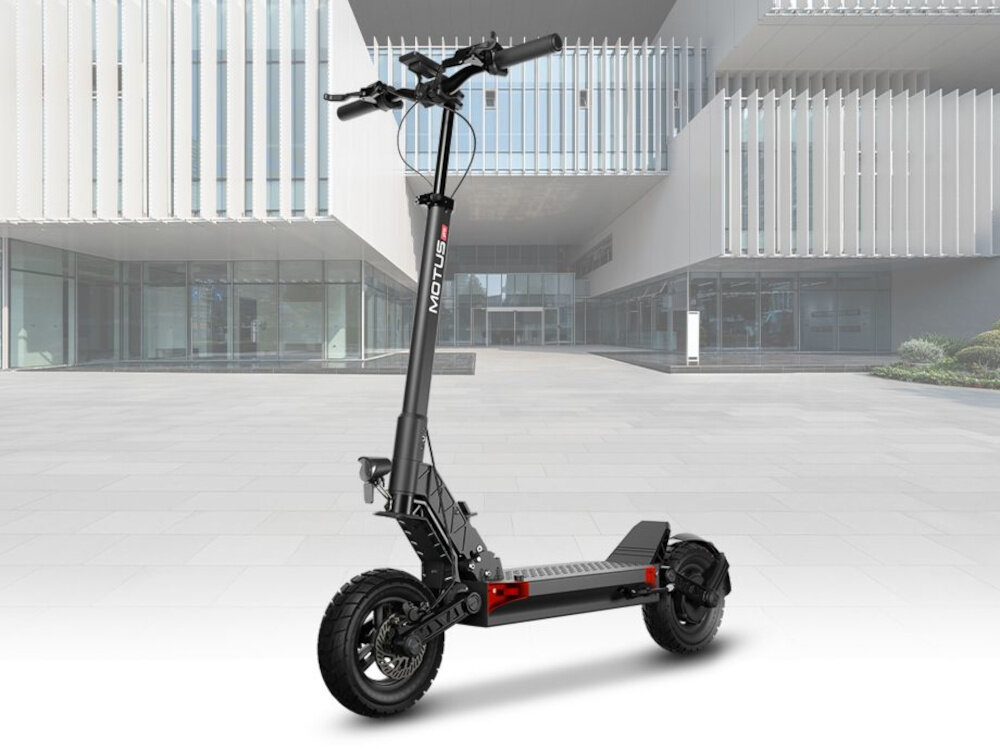 Hulajnoga elektryczna MOTUS Pro 10 70km 1000W 2 amortyzatory 10 cali Czarny hulajnoga na tle budynku widoczna od przodu pod skosem styl stabilność do miasta