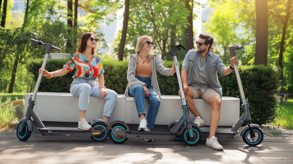 Hulajnoga elektryczna MOTUS Scooty 10 Plus Gen 6 65km 500W Amortyzacja 10 cali Szary trzy osoby siedzą na ławce każda osoba trzyma swoją hulajnogę za kierownicę w tle drzewa i krzewy środek transportu styl zabawa jazda na hulajnodze stabilność wygoda aplikacja
