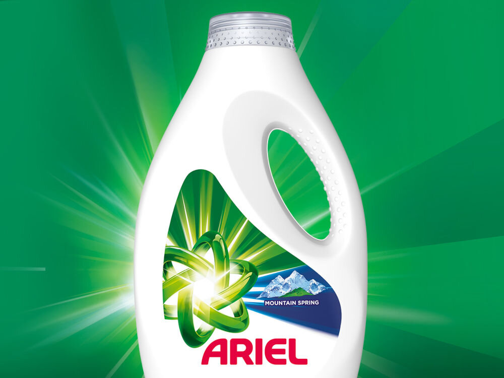 Płyn do prania ARIEL Mountain Spring 2250 ml do kolorowych tkanin Biała butelka płynu do prania ARIEL Mountain Spring z zielonym symbolem atomu na tle rozchodzących się promieni świetlnych