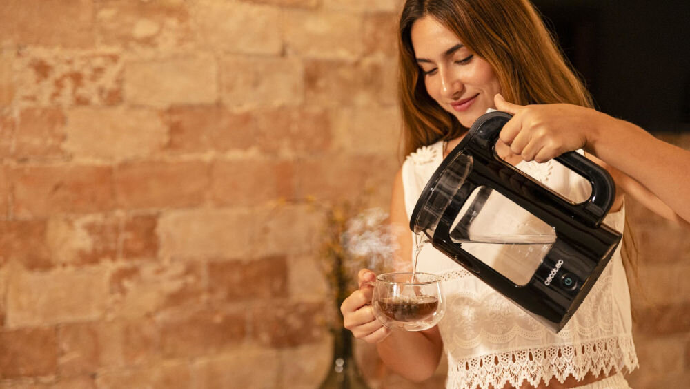 Czajnik CECOTEC ThermoSense 330 Glassy kobieta trzyma czarny czajnik przeźroczysta szybka kobieta nalewa wodę do filiżanki moc 2200 W zagotowanie wody w zaledwie kilka chwil herbata kawa funkcja Keep Warm utrzymuje temperaturę nawet do 2 godzin praktyczne rozwiązanie 