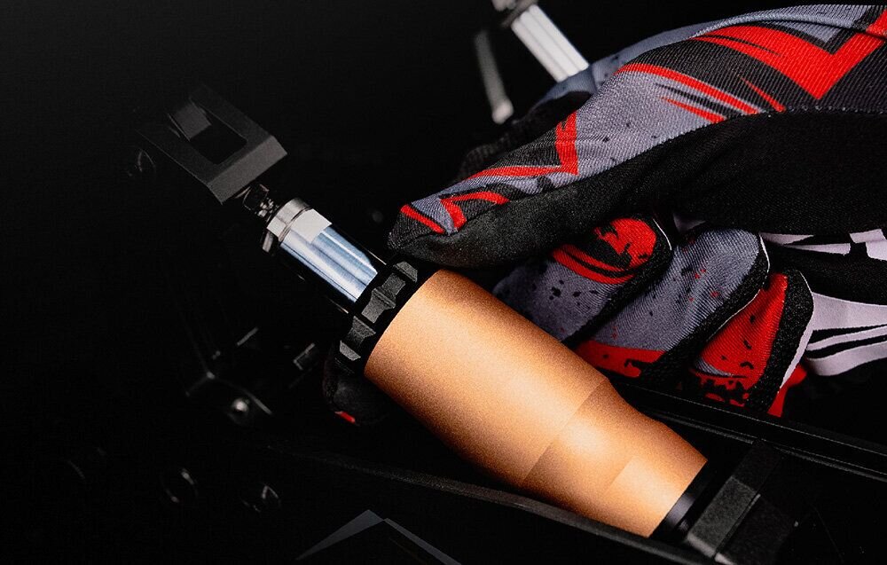 Zestaw MOZA Racing CRP2 RS066 prezentacja Dłoń w rękawicy wyścigowej trzymająca metalowy cylinder tłumika pedałów Moza CRP2, co prezentuje łatwy dostęp do komponentów i sportowy charakter akcesoriów regulowany pedał gazu i sprzęgła dostosowanie oporu komfort użytkowania system beznarzędziowej regulacji