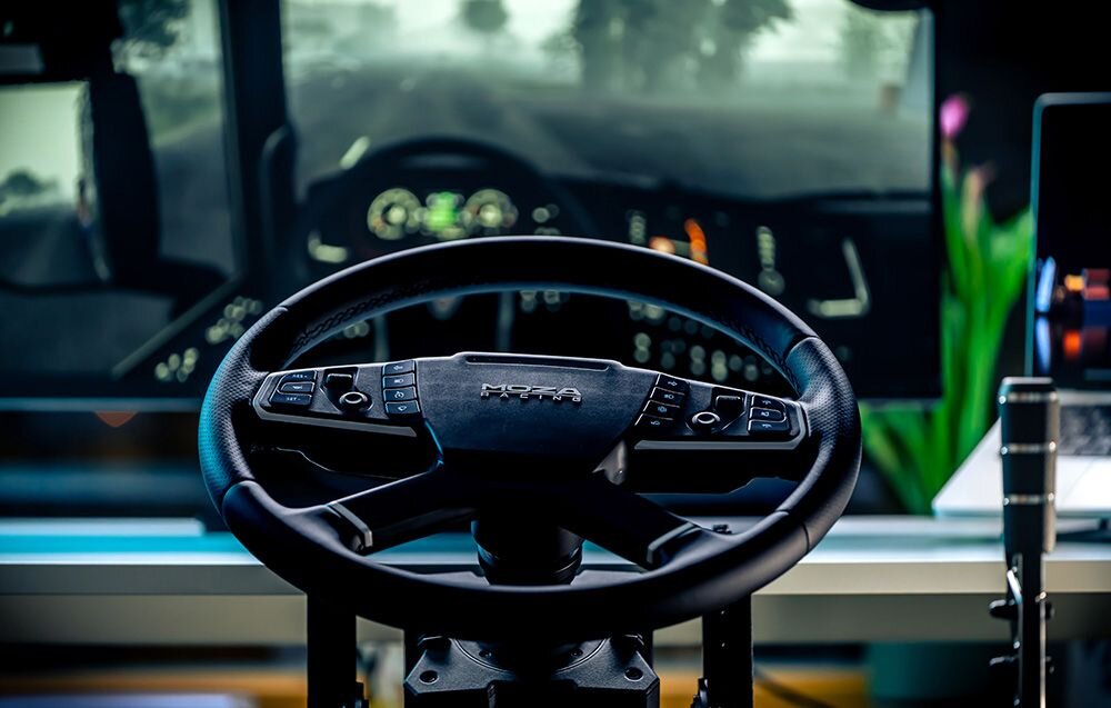 Kierownica MOZA Racing TSW RS060 (PC) Widok zza kierownicy MOZA Racing na ekran monitora wyświetlający deskę rozdzielczą ciężarówki w symulatorze aluminiowe pokrętła, funkcja D-pad, kontrola parametrów, personalizacja sterowania