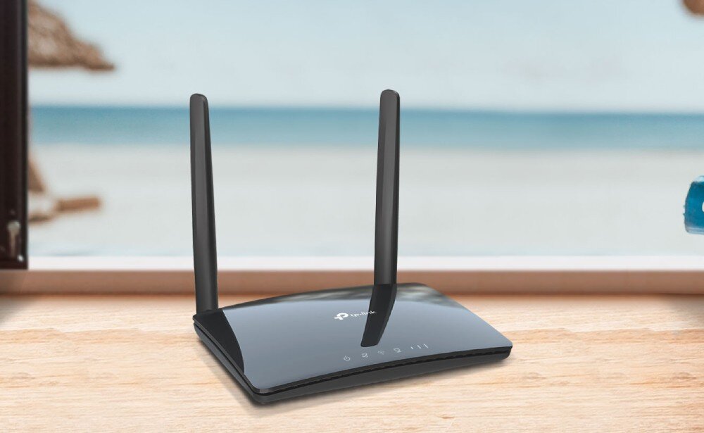 Router TP-LINK Archer MR402 Czarne urządzenie z dwiema pionowymi antenami stoi na drewnianym blacie przy otwartym oknie, za którym widać plażę i morze, opis
