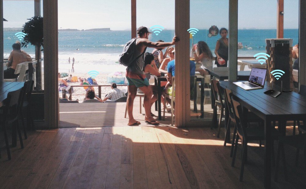 Router TP-LINK Archer MR402 Wnętrze kawiarni z widokiem na plażę, przy stolikach siedzą ludzie, a w powietrzu widać symbole sygnału Wi-Fi połączone z urządzeniem na stole, anteny, sieć, sygnał