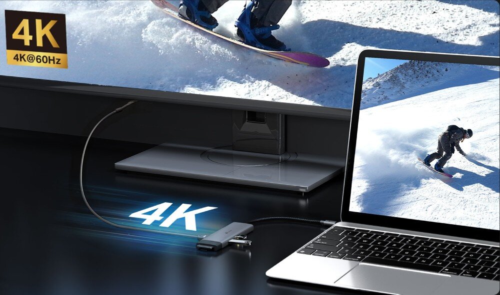Hub TP-LINK UH7020C Laptop połączony za pomocą adaptera z dużym monitorem, na którym wyświetlany jest film ze snowboardzistą, z nałożonym napisem '4K' oraz informacją '4K@60Hz'