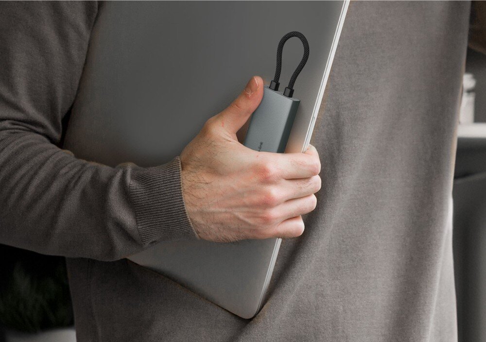 Hub TP-LINK UH7020C Dłoń trzymająca zamkniętego laptopa wraz z niewielkim, szarym adapterem, co obrazuje kompaktowy rozmiar urządzenia