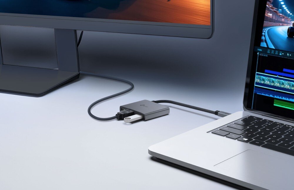 Hub TP-LINK UH3020C Srebrny adapter podłączony kablem w oplocie do laptopa, z wpiętym pendrivem i kablem wideo prowadzącym do monitora zewnętrznego na jasnym blacie