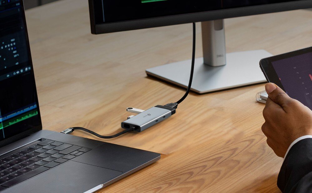 Hub TP-LINK UH5020C Podłużny szary adapter podłączony do boku laptopa za pomocą plecionego kabla, przekazujący sygnał wideo do dużego monitora zewnętrznego na drewnianym biurku