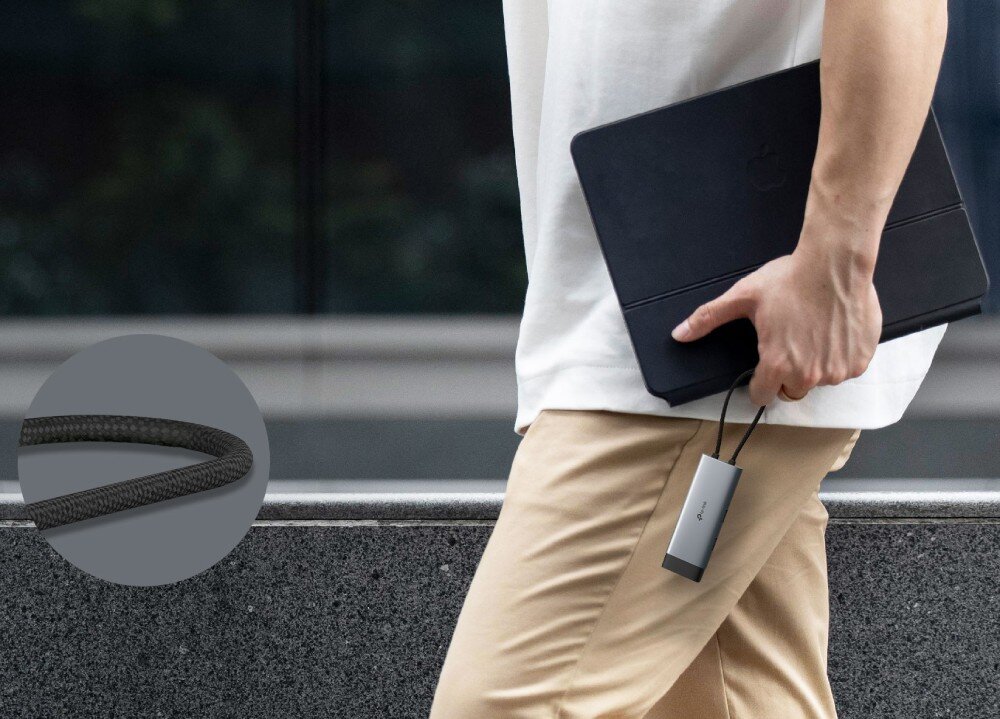 Hub TP-LINK UH5020C Osoba idąca z czarnym tabletem w etui, trzymająca w dłoni szary adapter za jego krótki przewód, w tle zbliżenie na splot czarnego oplotu kabla