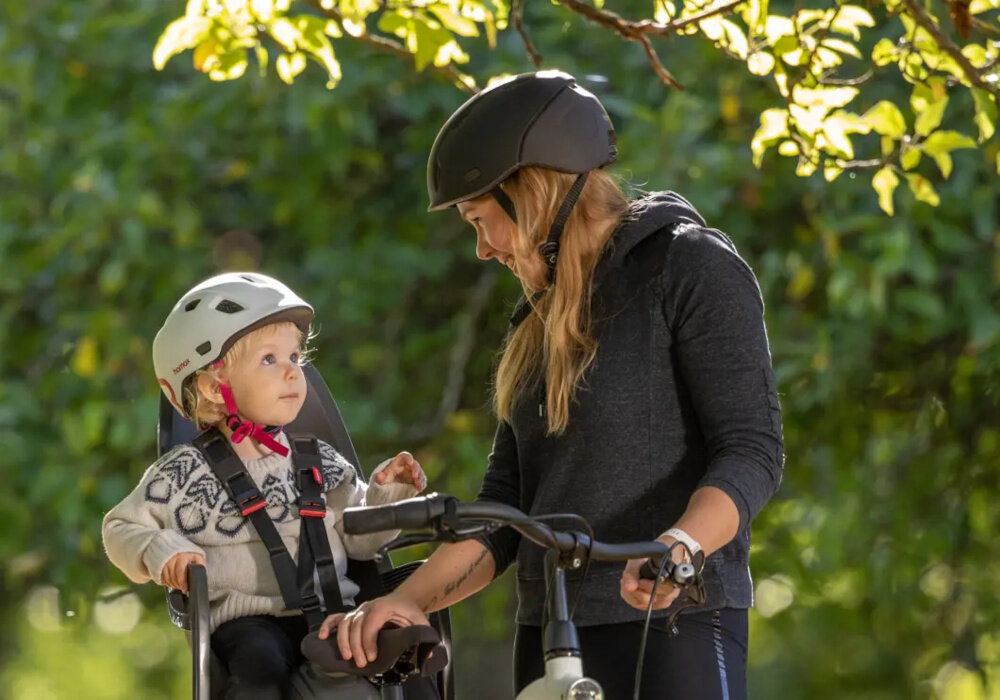 Fotelik rowerowy HAMAX Zenith Relax Relax Adapter Szaro-czerwony park las drzewa dziecko w foteliku siedzi zapięte fotelik na rowerze rower trzyma dorosła osoba bezpieczna podróż wygoda przyjemność