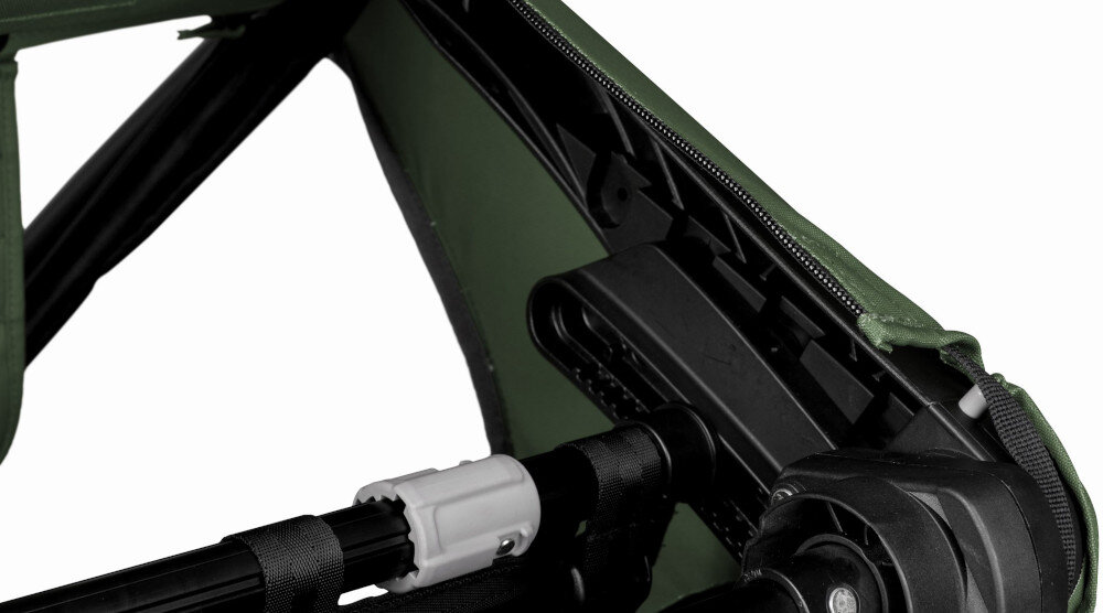 Zbliżenie na mechanizm przyczepki rowerowej z widocznymi elementami konstrukcyjnymi w kolorze zielonym i czarnym. Widać zamek błyskawiczny oraz części metalowe i plastikowe.