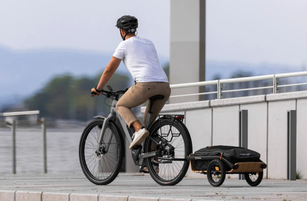 Przyczepka rowerowa HAMAX Venture+ 400702 osoba na rowerze jedzie po ulicy z przyczepioną przyczepką transport bagażu praktyczność funkcjonalność