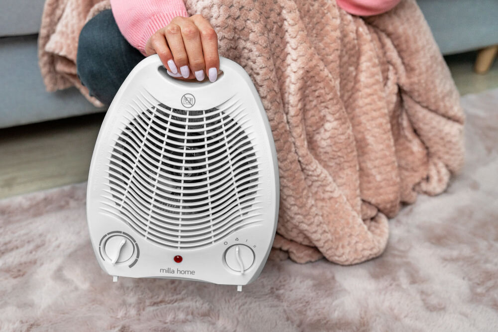 Termowentylator MILLA HOME MFH103 Zbliżenie na dłoń trzymającą za wygodny uchwyt biały termowentylator przenośny MILLA HOME MFH103.