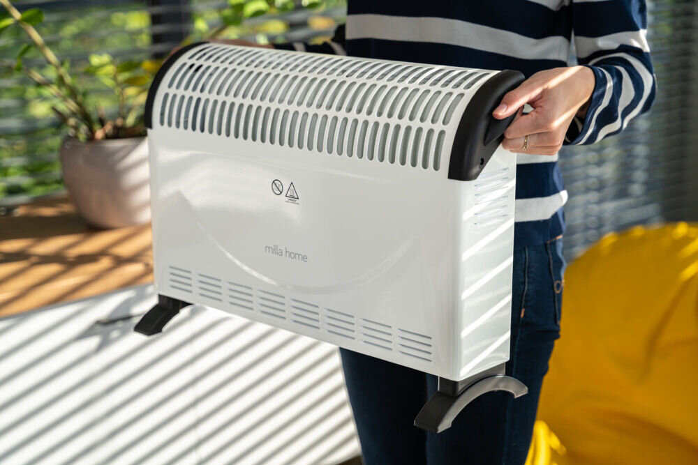 Grzejnik konwektorowy MILLA HOME MCH103 grzejnik przenoszony przez kogoś trzymany za uchwyty