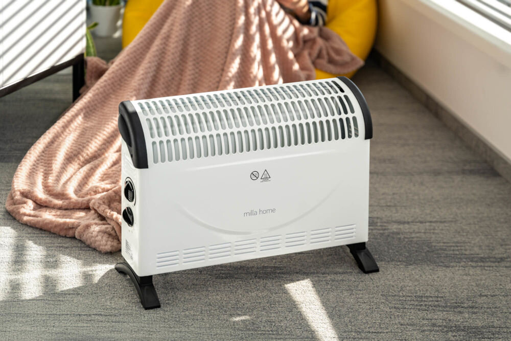 Grzejnik konwektorowy MILLA HOME MCH103 system zabezpieczający grzejnik stojący w tle fotel nakryty kocem