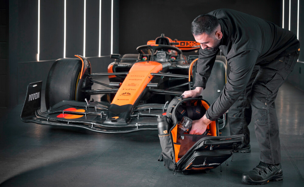 Plecak monterski DEWALT McLaren F1 DWST60101-9 pomieszczenie osoba wkłada wiertarkę do plecaka otwarty plecak w tle samochód McLaren mobilność porządek w pracy do pracy w każdym miejscu wygoda porządek szybki dostęp do narzędzi