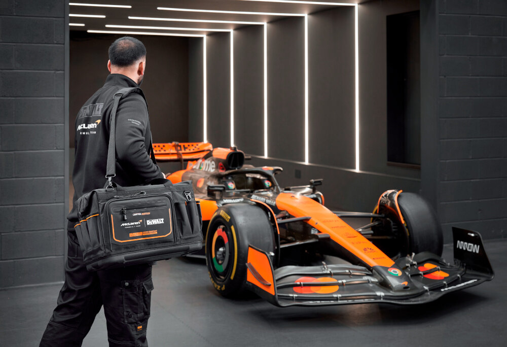 Torba narzędziowa DEWALT DWST60104-9 osoba niesie torbę przewieszoną przez ramię w tle samochód McLaren mocny pasek komfortowe przenoszenie na ramieniu pojemność 48,7 litra maksymalne obciążenie do 20 kg pełna mobilność wymiary 31 x 50,8 x 29 cm