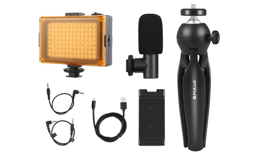 Na obrazie znajduje się zestaw do nagrywania, w skład którego wchodzą: lampa LED z pomarańczowym filtrem, mikrofon z gąbką, statyw z logo \'PULUZ\', dwa kable audio, kabel USB oraz uchwyt na baterie.