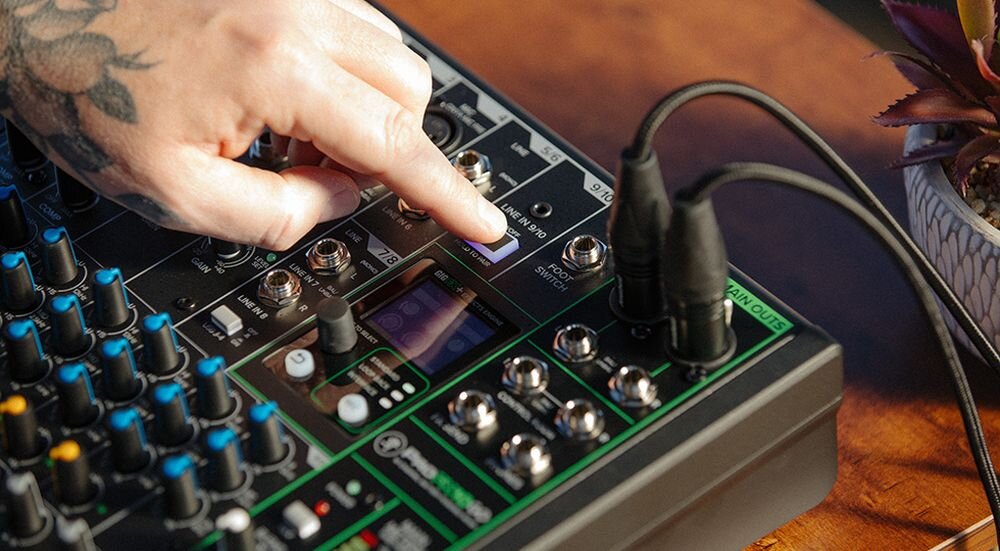 Mikser audio MACKIE ProFX10 GO Bluetooth dwukierunkowy streaming rozmowy Mix Minus, ręka trzymająca guzik, mikser stojący na stole