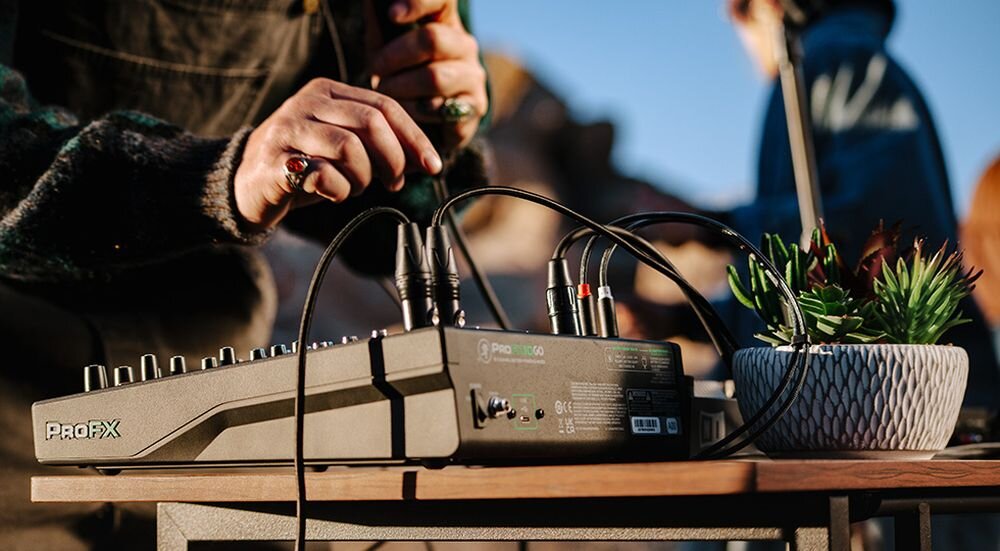 Mikser audio MACKIE ProFX10 GO wejścia wyjścia odsłuch słuchawkowy system nagłośnienia, mikser stojący na stole, osoba stojąca przy mikserze