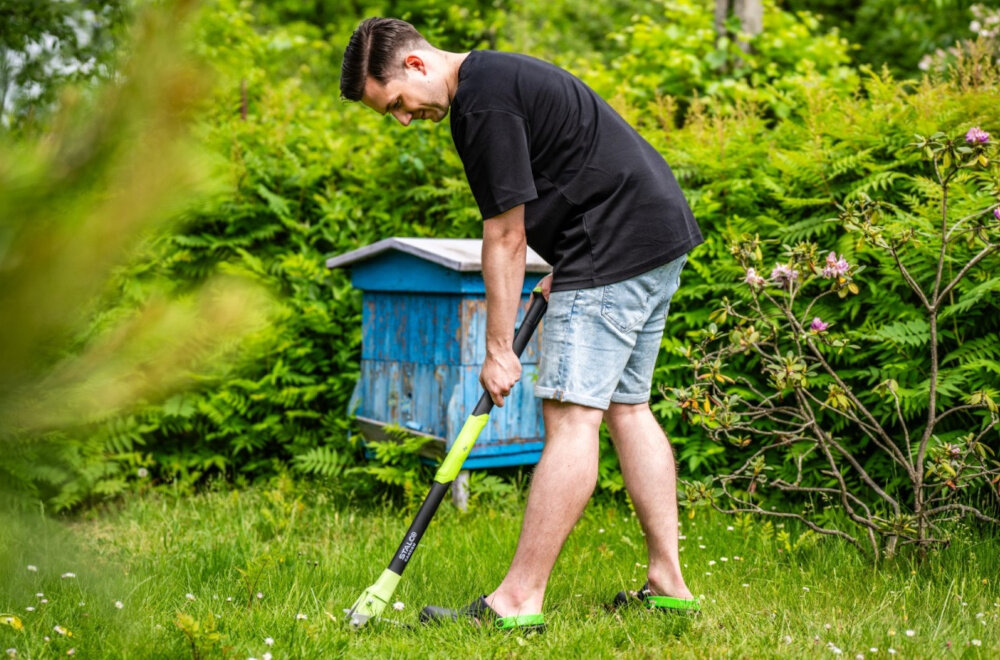 Wyrywacz do chwastów STALCO GARDEN EXP S105210372 ogród osoba wyrywa chwast z trawnika w tle niebiski ul rośliny aluminiowy trzonek o długości 100 cm praca w pozycji stojącej niska waga całkowita około 950 g aluminium jest odporne na wilgoć i zmienne warunki atmosferyczne