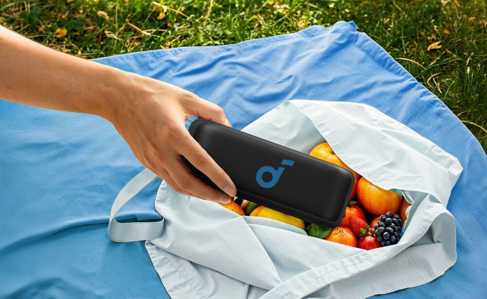 Głośnik mobilny SOUNDCORE Select 2S przenośna kompaktowa konstrukcja, osoba wkładająca głośnik do torby z owocami