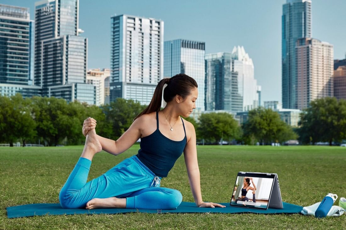 Kobieta praktykująca jogę w parku, laptop umieszczony obok niej na trawie, w tle drzewa i trawa. - procesor Intel Core Ultra, pamięć RAM, Dysk SSD  
