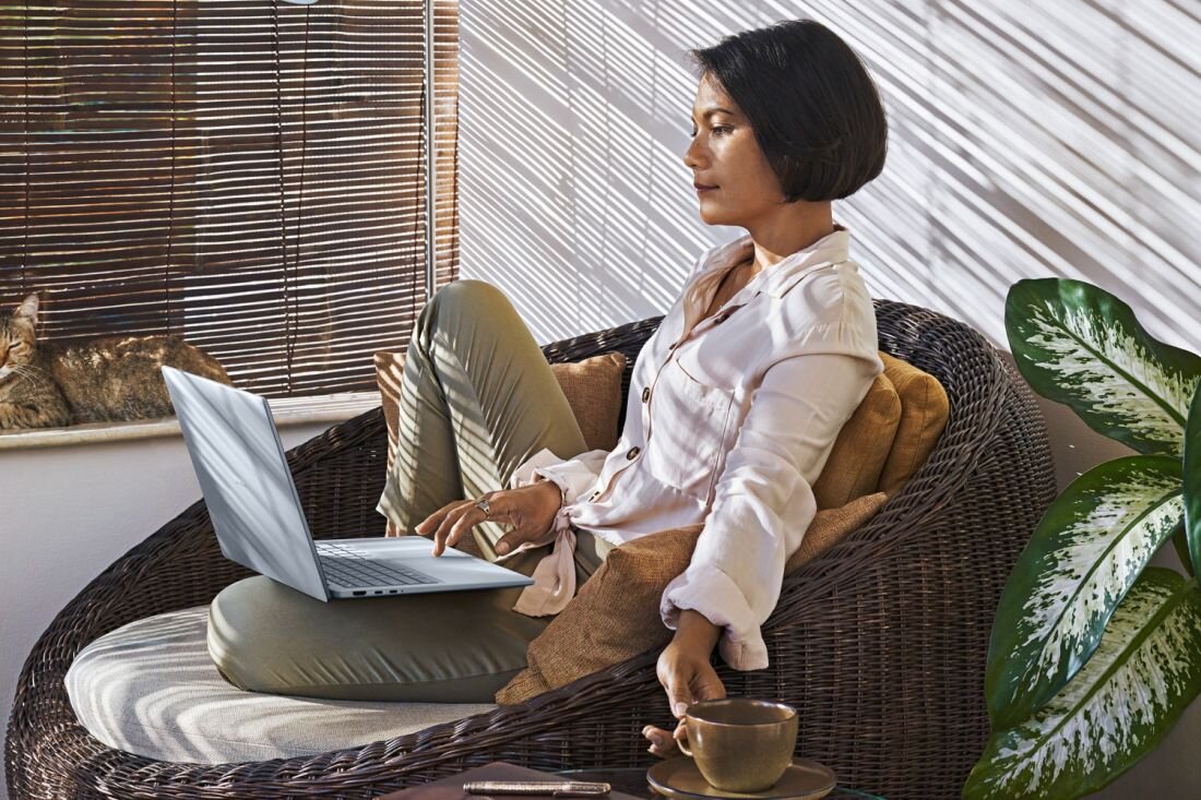 Kobieta siedzi na wiklinowym krześle, pracując na laptopie DELL 14 Plus. - aplikacja MyDell