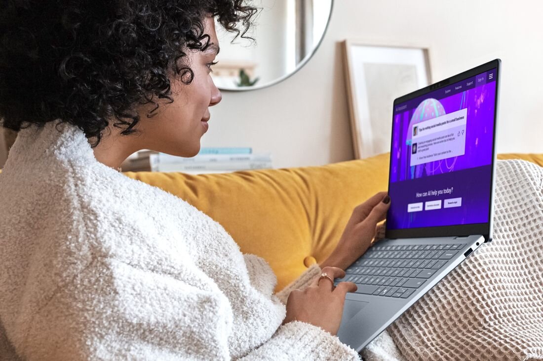 Kobieta w szlafroku relaksuje się na kanapie, korzystając z laptopa DELL 14 Plus, z uśmiechem na twarzy.  - Copilot i jego funkcje