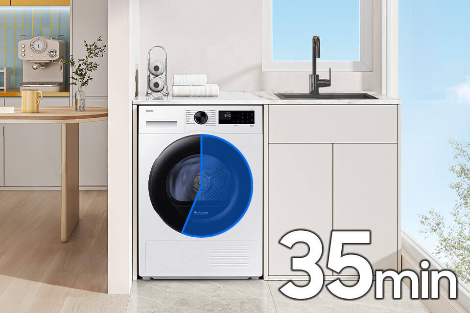 Na obrazie znajduje się biała suszarka z czarnym i niebieskim elementem na drzwiach, umieszczona w kuchni obok zlewu. Na dole widoczny jest napis \'35 min\'.