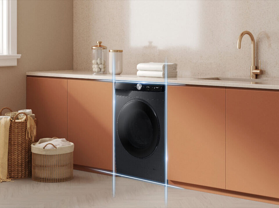 Pralka Slim WW90DG6G94LBU4 EccoBubble Czarna pralka w zabudowie kuchennej z brązowymi szafkami i jasnym blatem. Obok pralki znajdują się kosz wiklinowy i złożone ręczniki.