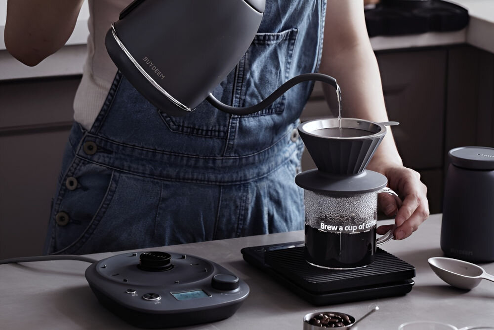 Czajnik BUYDEEM K821 Szary czajnik gęsia szyjka szary podstawka przyciski osoba trzyma czajnik i wlewa wodę do karafki gęsia szyjka lata 50-te styl vintage unikalna kolorystyka struktura retro design elegancja pojemność 800 ml stylowy wygląd funkcjonalność ergonomiczny uchwyt wygoda precyzyjna wylewka kontrolowanie nalewania wody dla miłośników retro praktyczne rozwiązania 