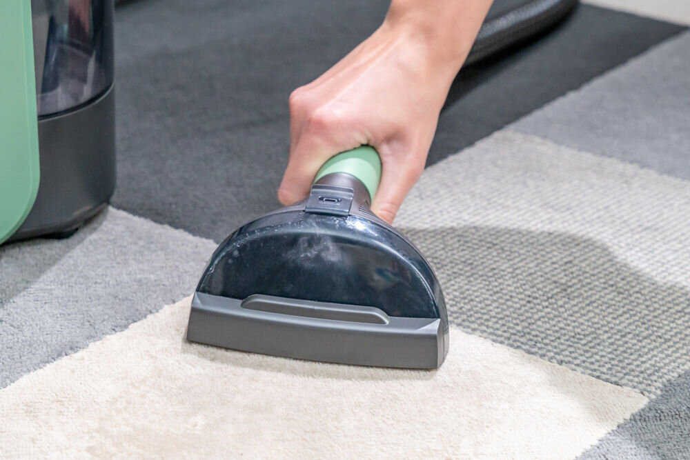 ODKURZACZ PIORĄCY SPOTCLEAN GOTZE&JENSEN CSC600 ze szczotką uniwersalną szeroką do butów do czyszczenia tapicerki meblowej samochodowej dywanów Zbliżenie na rękę kobiety używającej dużej ssawki do prania jasnego fragmentu dywanu.