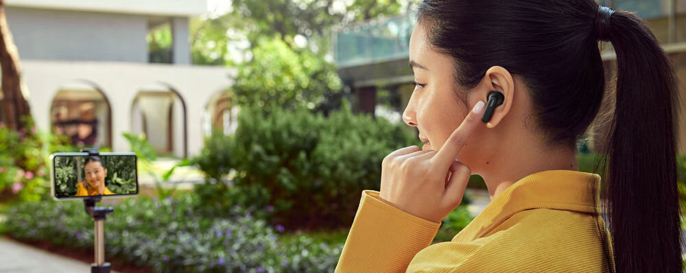 Słuchawki OPPO Enco Buds3 Pro sterowanie dotykowe robienie zdjęć kontrola muzyki, osoba z założonymi słuchawkami dokanałowymi, smartfon włożony w selfie stick