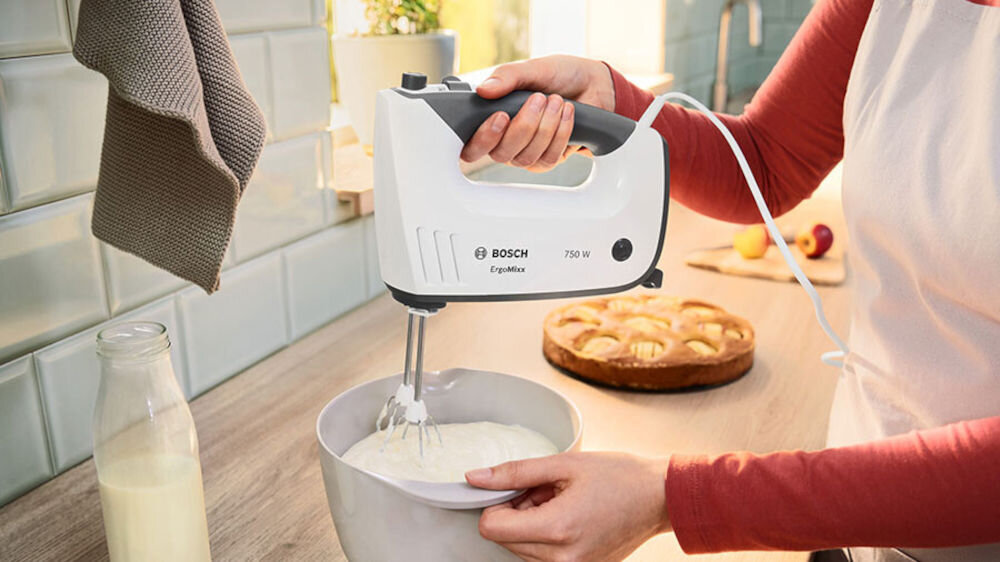 Mikser BOSCH ErgoMixx MFQ37490 Biały osoba trzyma mikser biało szara obudowa ubija masę ergonomiczny uchwyt pokryty miękką powłoką pewny chwyt pełna kontrola nd urządzeniem zwiększona wygoda użytkowania zmniejszenie zmęczenia podczas pracy komfortowa praca z urządzeniem
