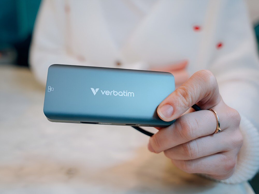 Hub Verbatim 32157 Osoba w jasnym swetrze trzyma w dłoni hub USB-C z widocznym logo producenta. Urządzenie skierowane jest portami w dół,
hub technologia gadżet adapter laptop komputer