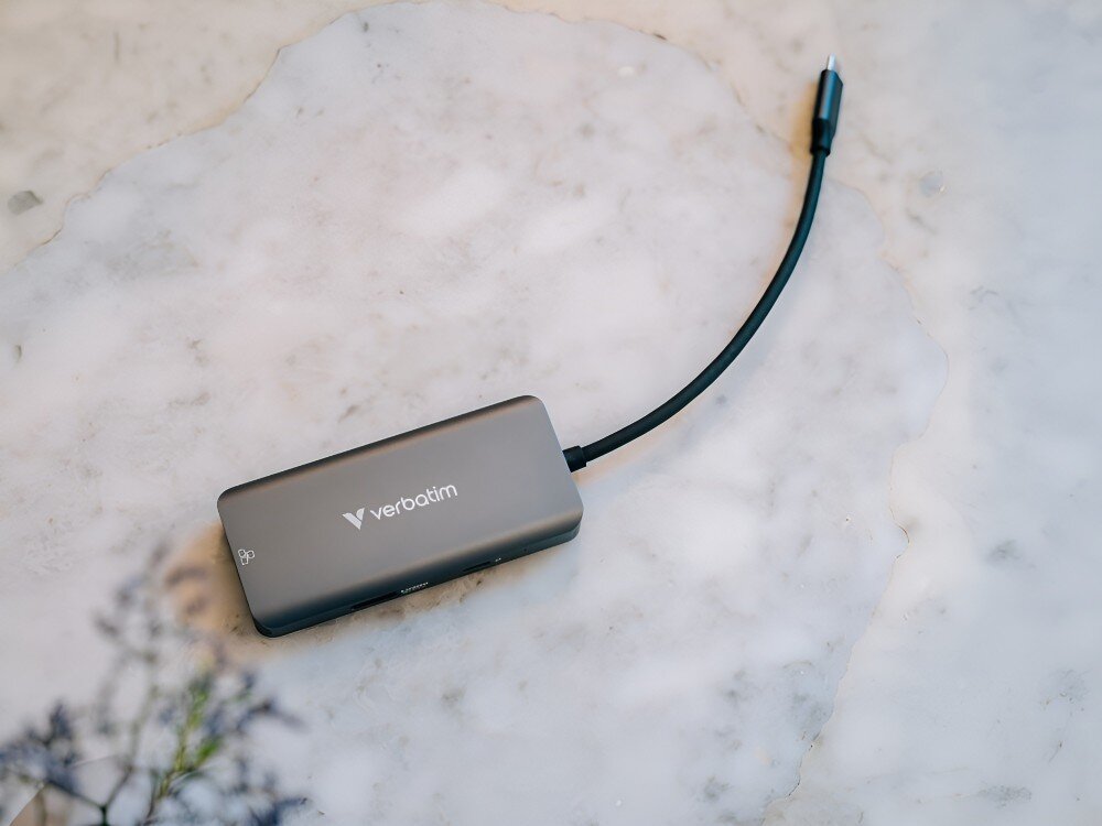 Hub Verbatim 32157 Hub USB-C z podłączonym kablem leży na marmurowym blacie. Obok widać rozmyte fragmenty rośliny,
hub usbc hdmi usba ethernet power delivery pd