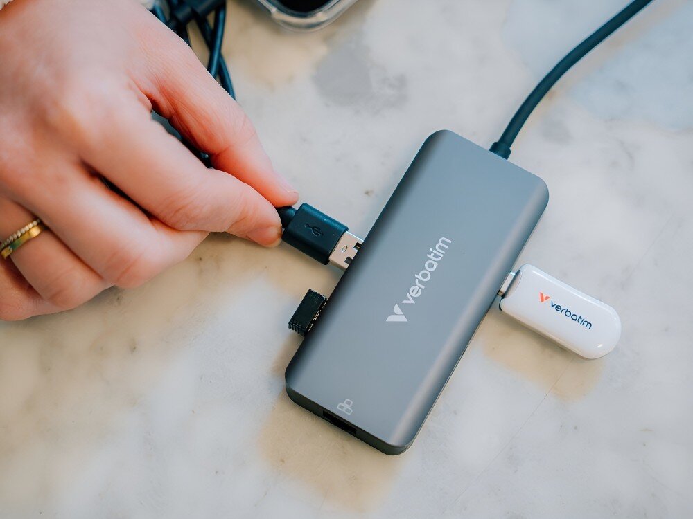 Hub Verbatim 32157 Zbliżenie na hub USB-C, do którego podłączone są pendrive i inne urządzenie przez port USB. Obok widoczna dłoń trzymająca wtyczkę,
hub usb power delivery pd 100w ładowanie zasilanie