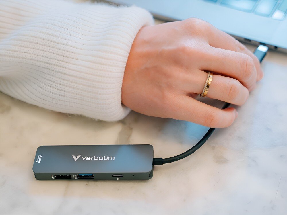 Hub Verbatim 32155 Hub USB-C podłączony do laptopa. Obok leży ręka osoby w białym swetrze,
usbc power delivery pd 100w zasilanie ładowanie